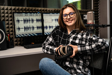 Portrait of female radio host with headphones and microphone in radio studio.