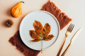 Brown leaf on a plate, decorative pumpkin and chestnut fruit on neutral beige background. Autumn concept. Top view, flat lay