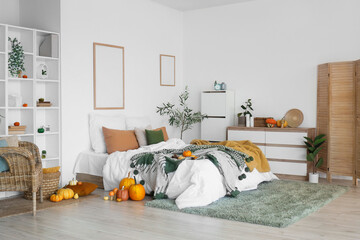 Interior of light bedroom with armchair, drawers and pumpkins