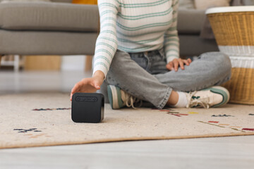 Beautiful young woman with wireless portable speaker sitting on floor at home