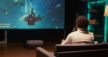 Gamer excited after winning game playing arcade space shooter on widescreen smart TV. BIPOC person...