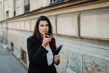 Young businesswoman sending voice message on smartphone on the street	

