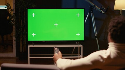Man using remote to zap through films available on streaming services on mockup TV. Person having movie night in home theatre using isolated screen television set, relaxing on couch