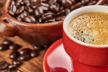 Cup of coffee in the foreground with roasted coffee beans and a cinnamon stick against a background of old wood