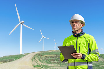 Technician with PPE inspecting wind turbines in a wind farm. Sustainability and renewable energy.
