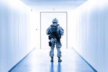Soldier standing in a bright hallway facing a closed door in full tactical gear with a strong backlight creating a tense mood  
