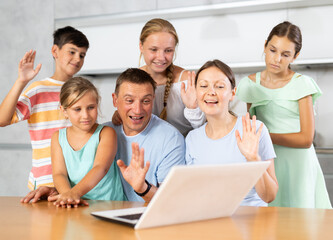 Obraz premium Large family with four kids are sitting in front of laptop and video chatting with friends, sharing news.