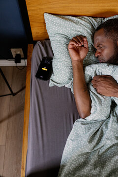 Man sleeping while alarm ringing on smartphone at eight o'clock in bed