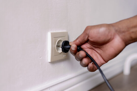 Partial close up of black man hand putting on wire in socket in room