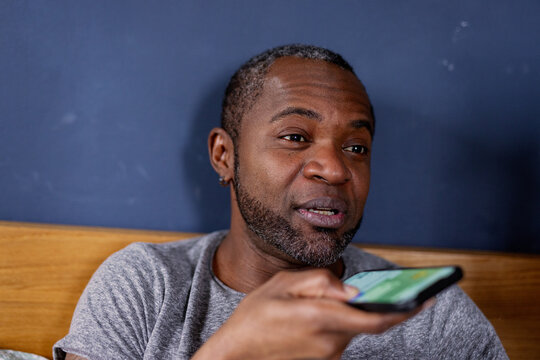 Adult black man recording audio message on smartphone in bed at home