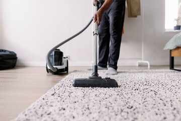 Partial view of man cleaning carpet with vacuum cleaner at home