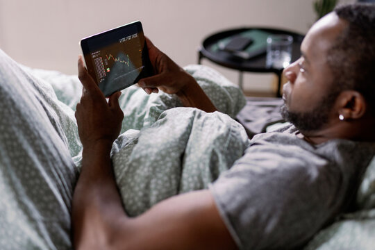 Side view of man watching stock market graph on digital tablet on bed
