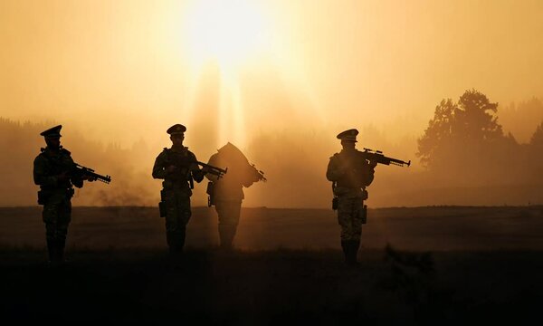 Silhouettes of army soldiers in the fog, with a glowing orange sunrise behind them, casting long shadows