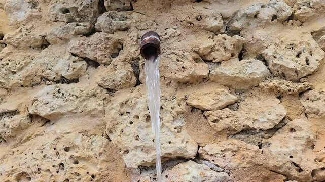 Old water tap leaking water with stone wall background. Water conservation or saving concept. Running water from old tap, consumption and usage concept.
