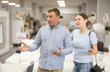Fototapeta premium Couple in store inspects upholstered furniture. They runs hand over soft fabric, imagining how it would look in living room, and wonders if its worth investment.