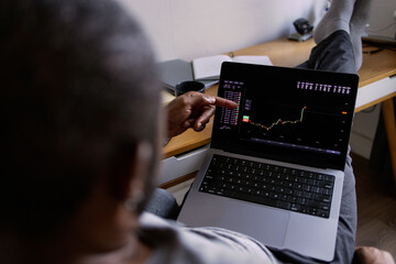 Partial man watching stock market graph on laptop in blurred room