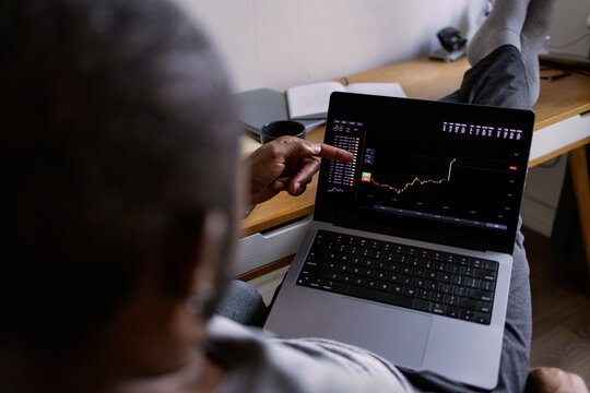 Partial man watching stock market graph on laptop in blurred room