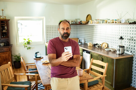 Middle aged man using smartphone in modern kitchen
