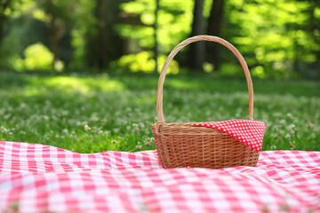 One picnic wicker basket with checkered napkin and blanket on green grass. Space for text