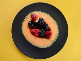 A cantaloupe with delicious strawberries and blackberries on a plate.