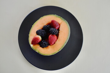 A cantaloupe with delicious strawberries and blackberries on a plate.