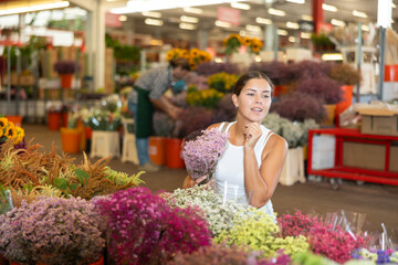 Glad young woman choosing bouquet of dry flowers in point of sale of plants