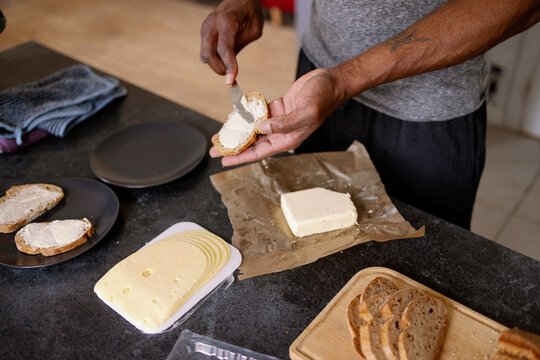 Cropped view of black man smearing butter with knife on bread slice