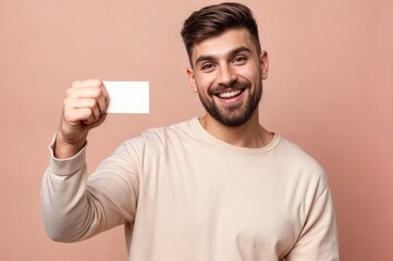 A smiling man in casual attire holds a blank card up towards the camera, posing in a cheerful studio setting with a peach background..