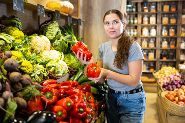 Obraz premium Young woman chooses bell pepper for purchase in vegetable shop