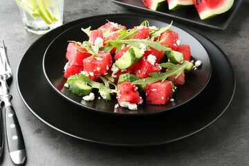 Delicious watermelon salad with feta cheese, cucumber and arugula served on grey textured table