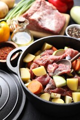 Cooking stew. Uncooked meat, vegetables and pot on black table, closeup