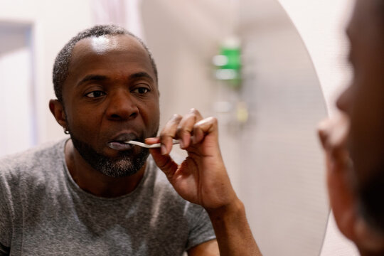 Focused black man looking at himself in mirror during brushing teeth