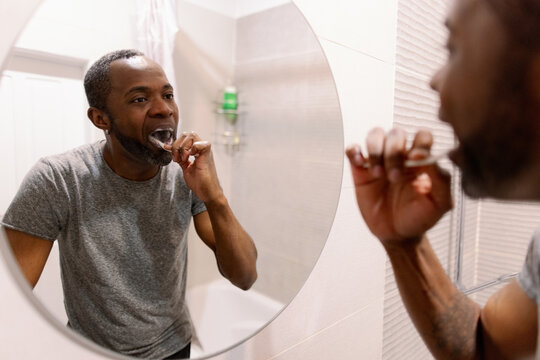 Mirror reflection and cropped view of man brushing teeth in bathroom