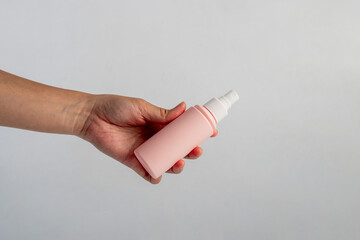 Cosmetic pink bottle and hand, bottle, lotion or serum with stylish props on white background. 