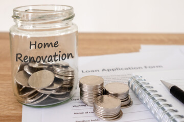 Coins in a glass jar for home renovation and loan application form on the wooden table. Borrowing money from the bank to renovate the house concept.