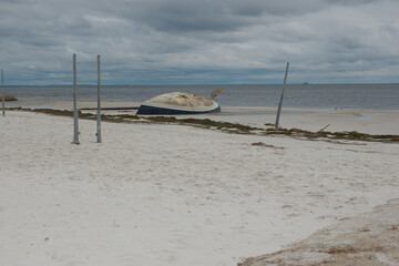 Blue and white Beached sailboat turned on its side on beach. After storm surge from Hurricane...