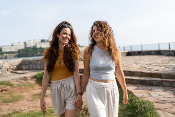 Two smiling women holding hands walking by the sea