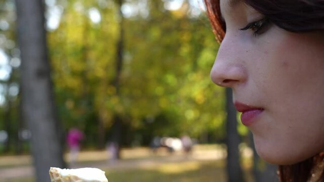 bold and daring teenage girl with a captivating, unconventional look seductively indulges in a creamy ice cream cone in a picturesque fall park, her tongue piercing adding a touch of edge.