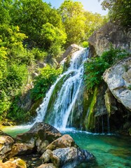 Obraz premium Crystal Clear Waterfall Cascading Down a Rocky Cliffside, Surrounded by Lush Green Trees and Vibrant Flora, Bathed in the Soft Light of Early Morning Sunshine