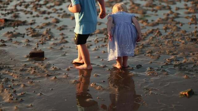 Two children walking barefoot on wet sand during low tide