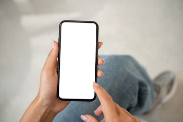 A woman in jeans sitting indoors and using her smartphone, with a white screen mockup displayed.