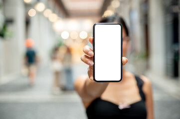 A woman showing a smartphone to the camera while standing in a market or mall.