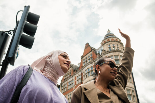 Low point of view of muslim woman and female friend hailing for a cab. - Powered by Adobe