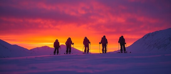 Fototapeta premium Five skiers stand in silhouette against a dramatic, colorful sunset in a snowy mountain landscape.