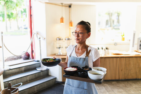Korean Waiter Approaching Table with Food in Restaurant