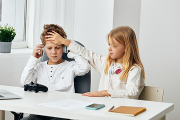 Happy Caucasian boy and girl studying elearning at home, sitting together at the living room table They are using their laptops, wearing headphones, and typing on their phones while playing