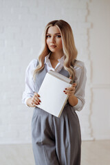 Young beautiful blonde in a gray suit and white shirt holding a book standing on a white background. The concept of professionalism, accountant or secretary.