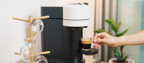hand making Espresso Coffee by Coffee Maker Machine with Capsule of roasted coffee bean on wood table bar. Daily beverage drink at Home, Apartment and Office concept