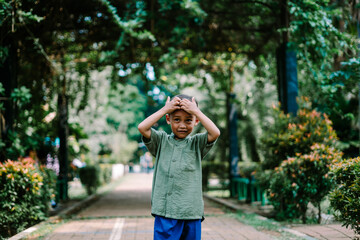 Naklejka premium A young Southeast Asian child holding their head, expressing discomfort or deep thought