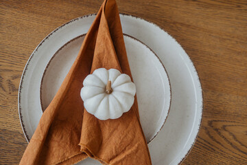 Fall table setting with a white pumpkin and brown napkin on a rustic wooden table